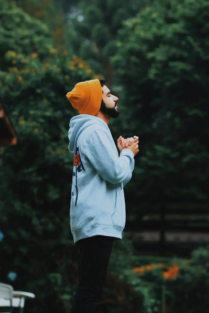 Services A man in a beanie and hoodie deeply praying outside in a lush green forest.