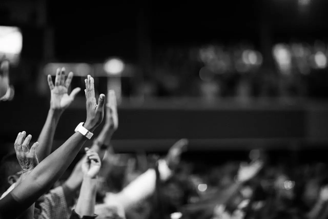 Services Black and white image of audience with hands raised, capturing concert energy.