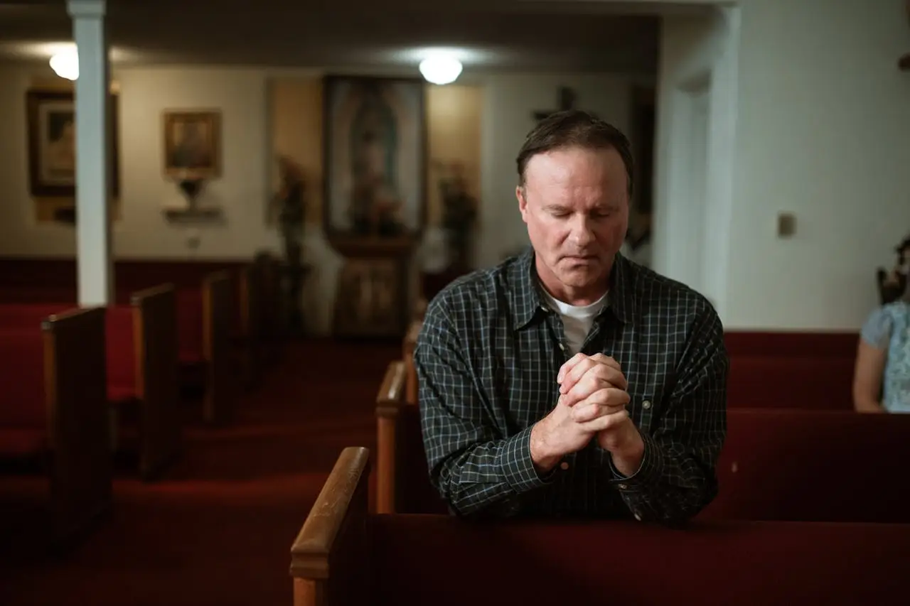 Services Adult man kneeling in church pew, praying with devotion in a quiet, sacred setting.
