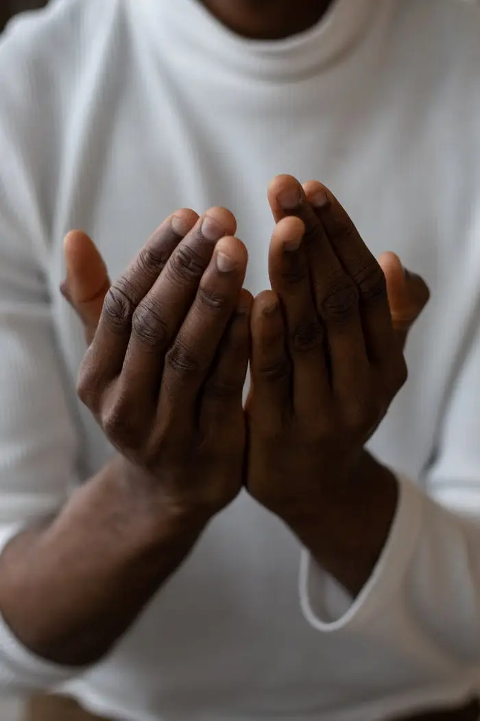 Services Selective focus of crop anonymous African American man wearing white turtleneck praying with open hands