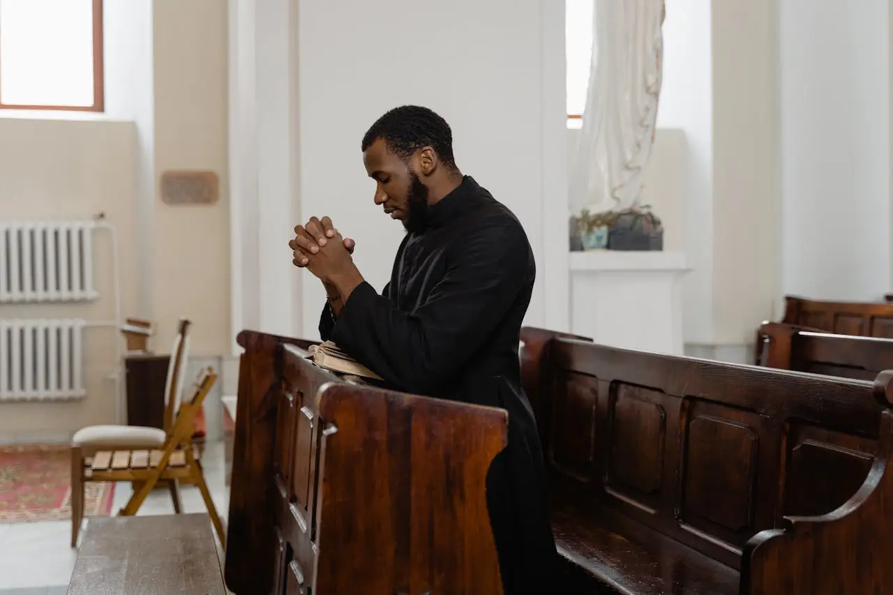 Contact A man in a cassock kneeling and praying in a church pew, expressing deep faith.